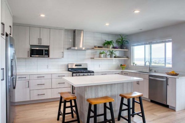 Bright modern kitchen with white cabinets, island, stools, and large window
