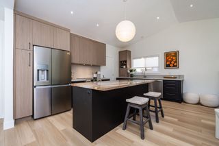 Modern kitchen with stainless steel appliances, black island, light wood cabinets, and two stools