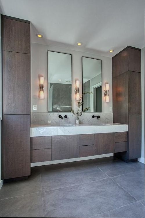 Modern double-sink bathroom vanity with dark wood cabinets, wall mirrors, sconces, and gray tile floor