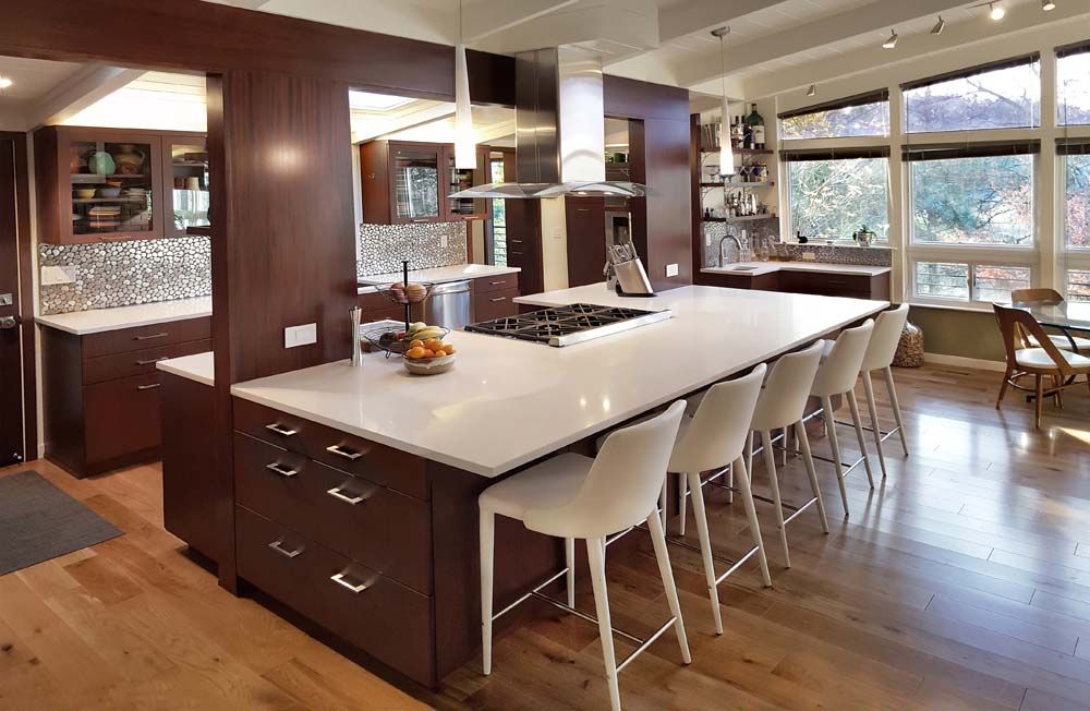 Modern kitchen with a large island, white countertops, bar stools, and hardwood floors with big windows.