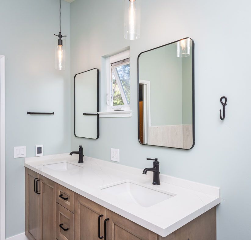Modern bathroom vanity with double sinks, black faucets, mirrors, and light blue walls.