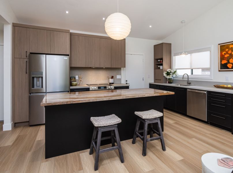 Modern kitchen with wood cabinets, stainless fridge, black island, two stools, and pendant light
