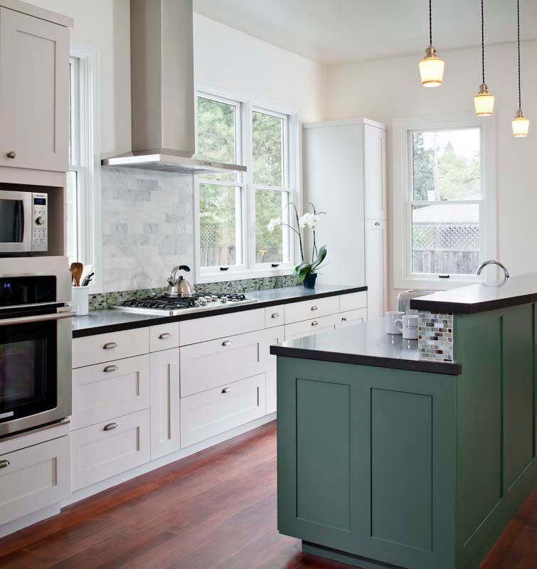 Bright modern kitchen with white cabinets, green island, pendant lights, and large windows