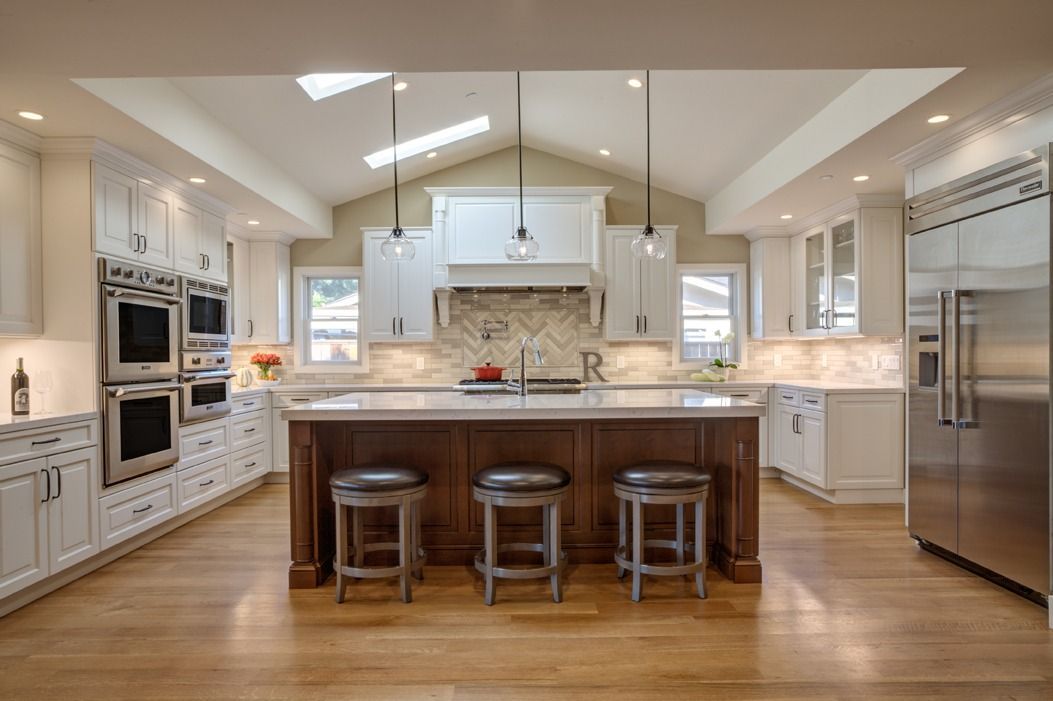 Bright modern kitchen with white cabinets, island seating, stainless steel appliances, and hardwood floors