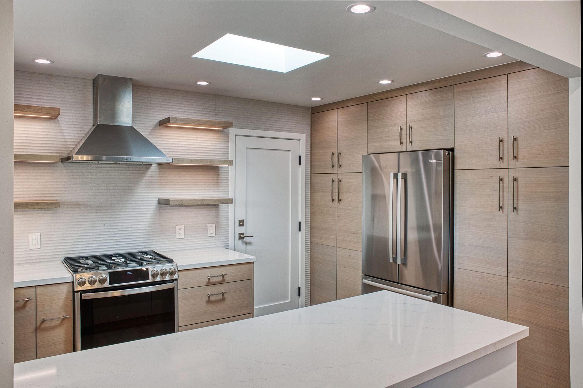 Modern kitchen with white island, stainless steel appliances, light wood cabinets, and tiled backsplash