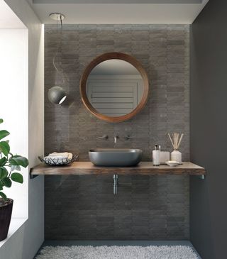 Modern bathroom vanity with gray tile, wooden shelf, round mirror, and vessel sink