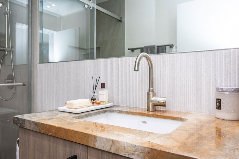 Modern bathroom vanity with stone countertop, sink, faucet, mirror, and glass shower doors