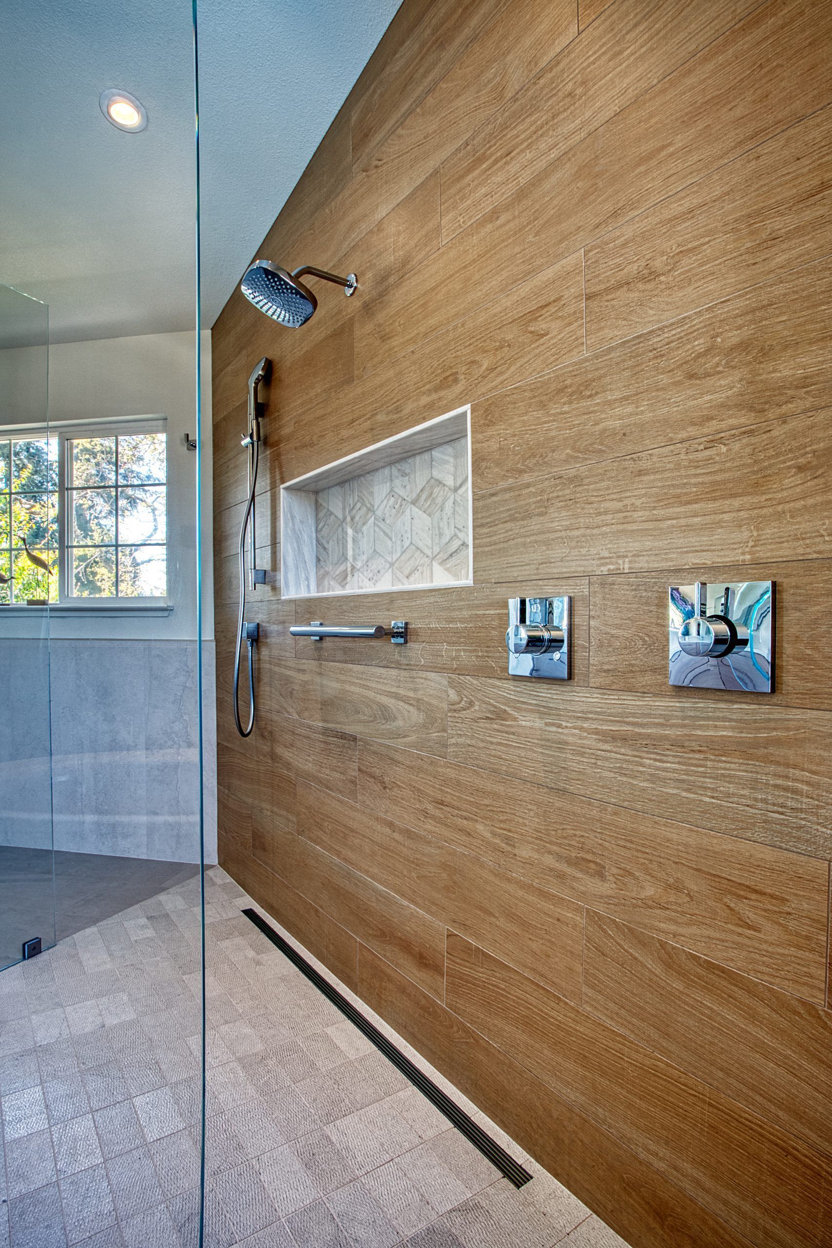 Modern bathroom shower with wood-look wall, glass window, and chrome fixtures