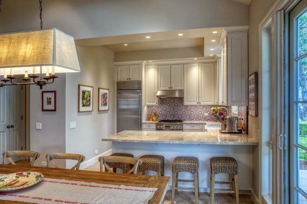 Bright kitchen with white cabinets, stone island, bar stools, and a dining area by large windows