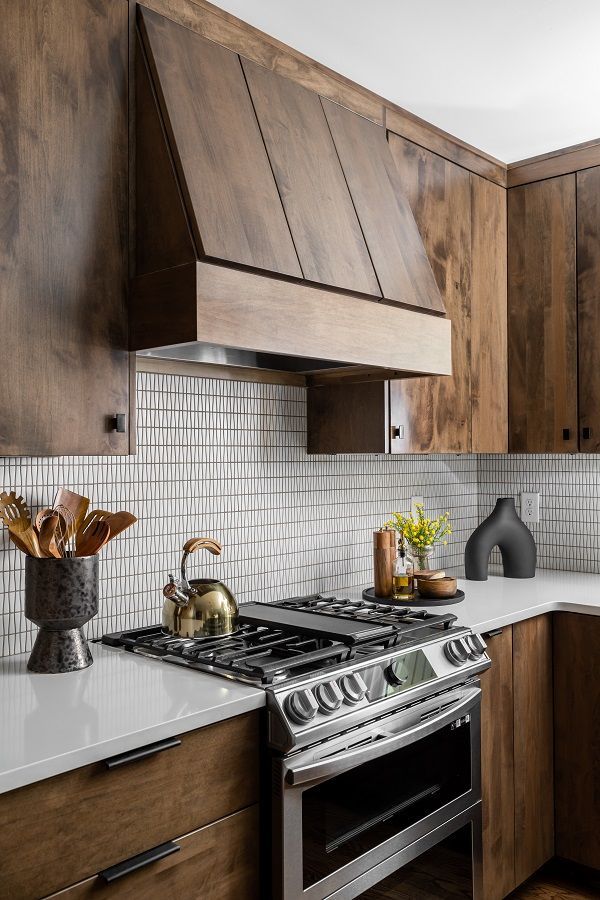 Modern kitchen with wood cabinets, white tile backsplash, gas range, and stainless-steel oven