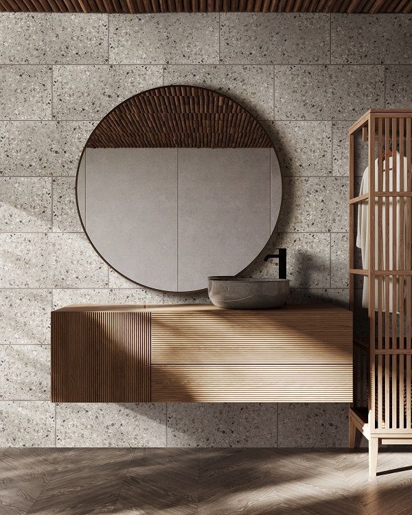 Modern bathroom vanity with round mirror, stone wall, and wooden slat cabinet.