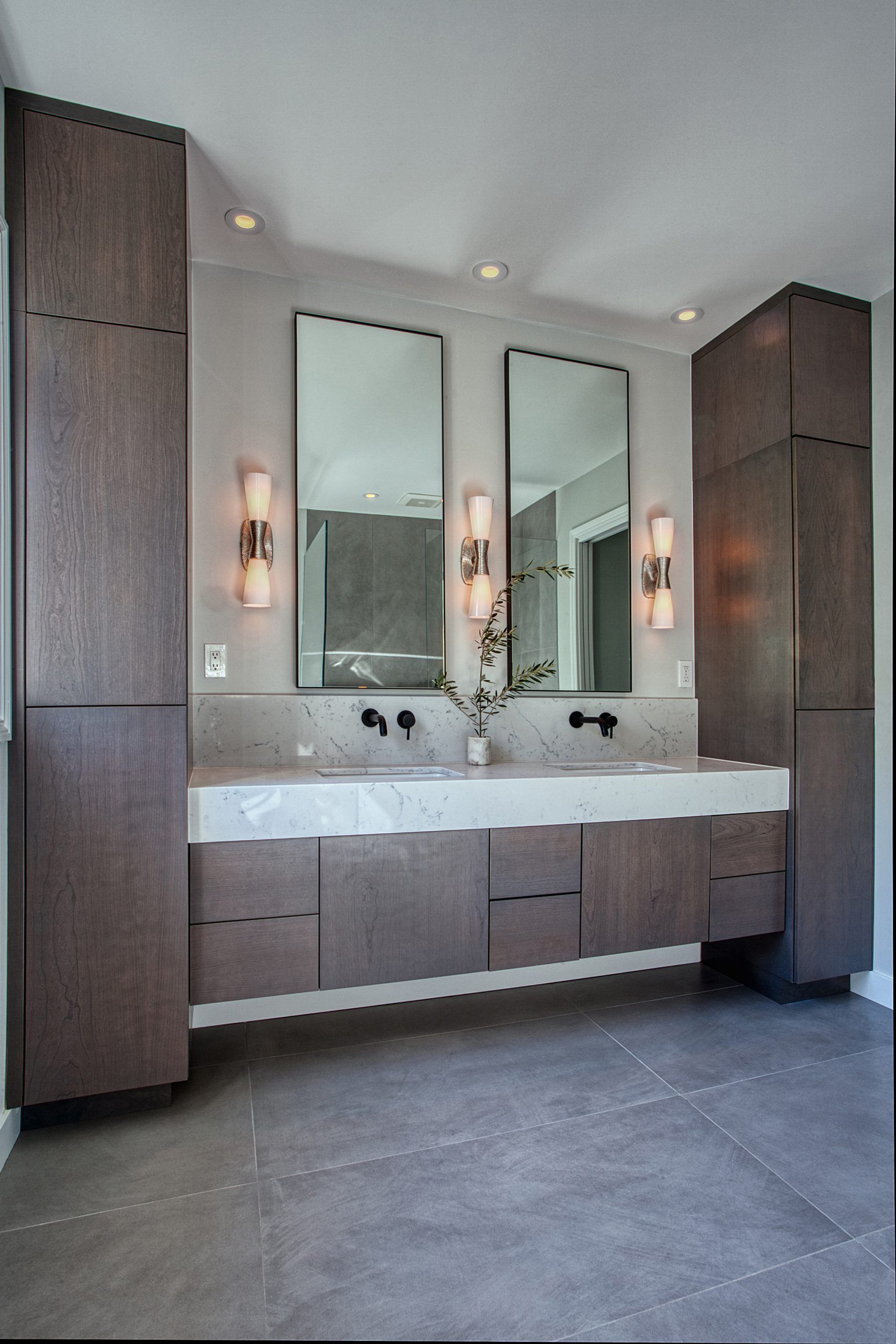 Modern bathroom vanity with double sinks, two mirrors, sconces, and tall wood cabinets
