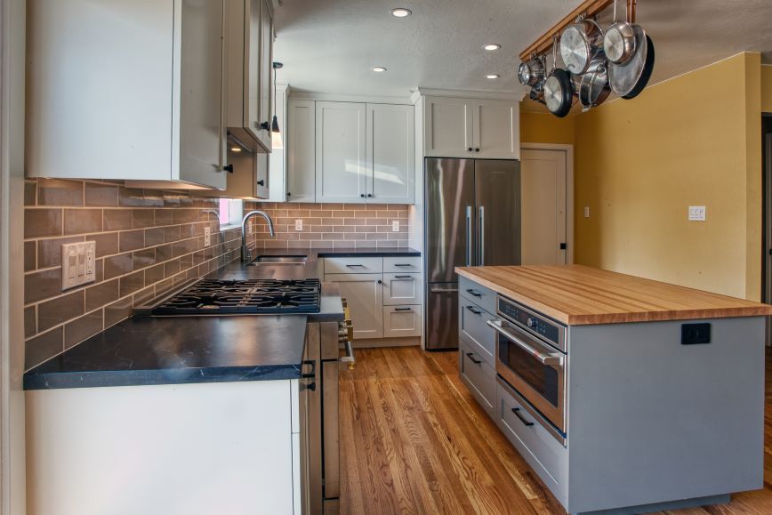 Modern galley kitchen with stainless steel appliances, white cabinets, wood floors, and a butcher-block island