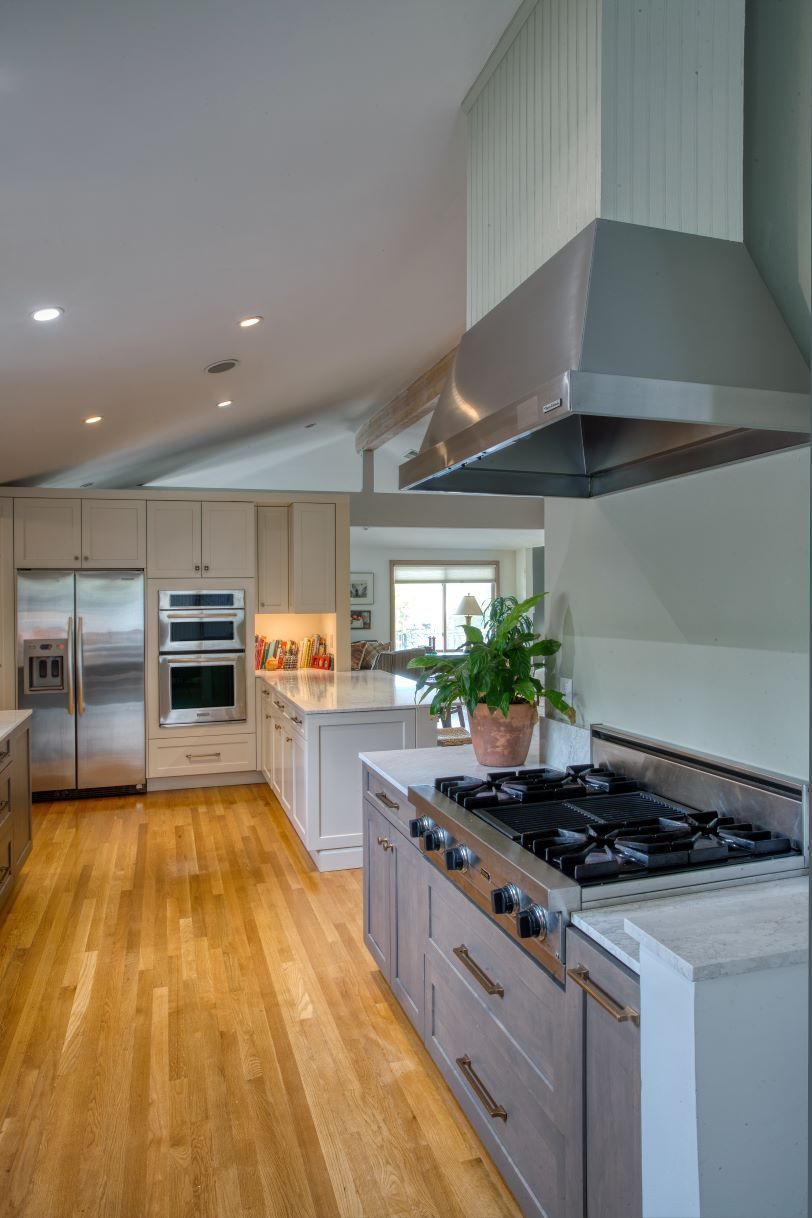 Modern kitchen with wood floors, stainless appliances, white cabinetry, and a gas range with hood.