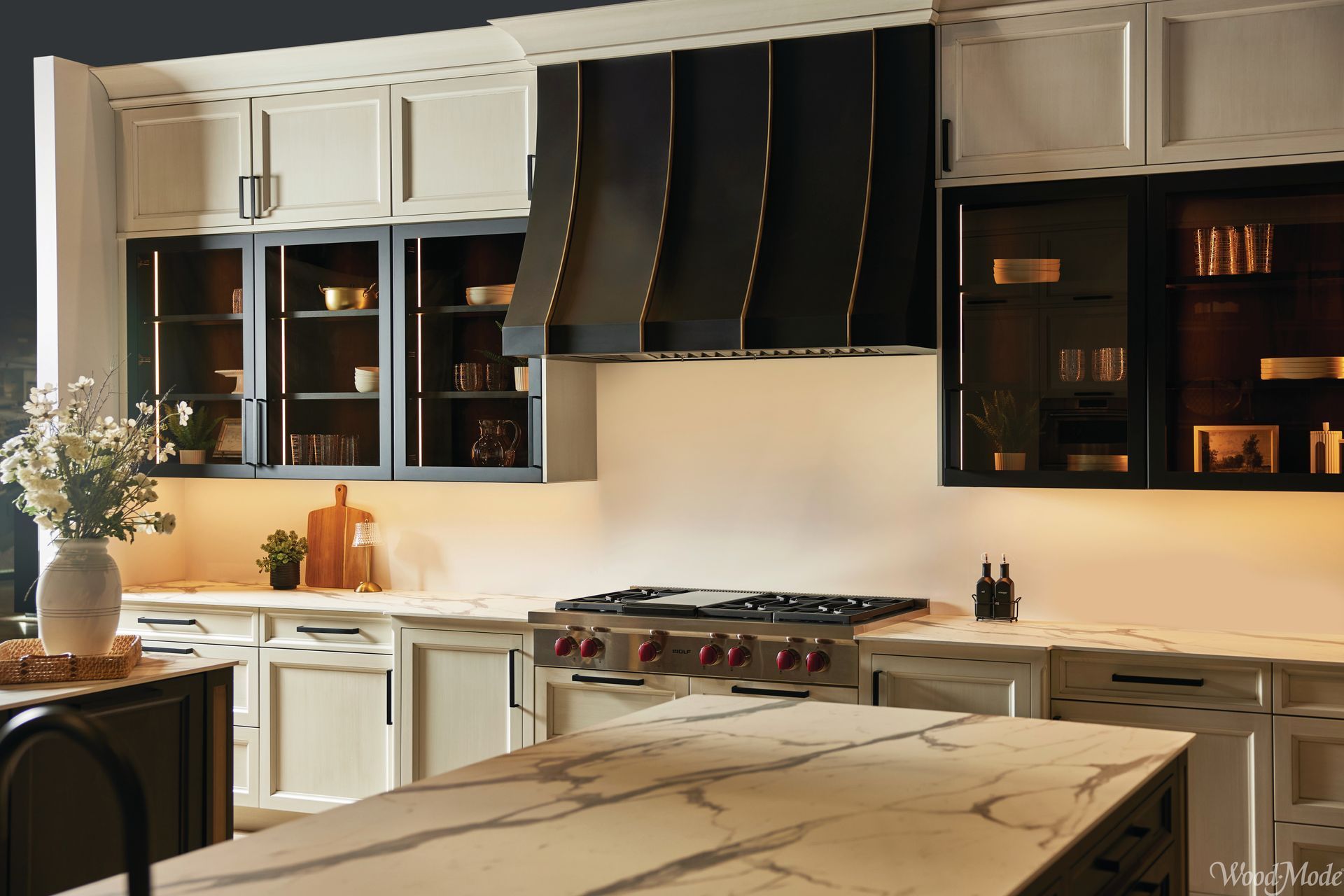Elegant white kitchen with dark accents, marble island, and a large stainless steel range hood
