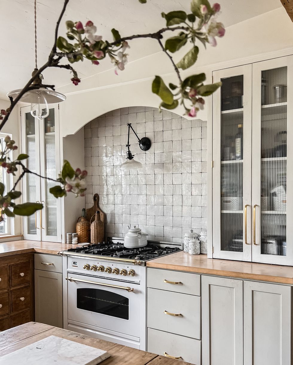Bright kitchen with white cabinets, wood countertops, tiled backsplash, and stove beneath floral branch decor