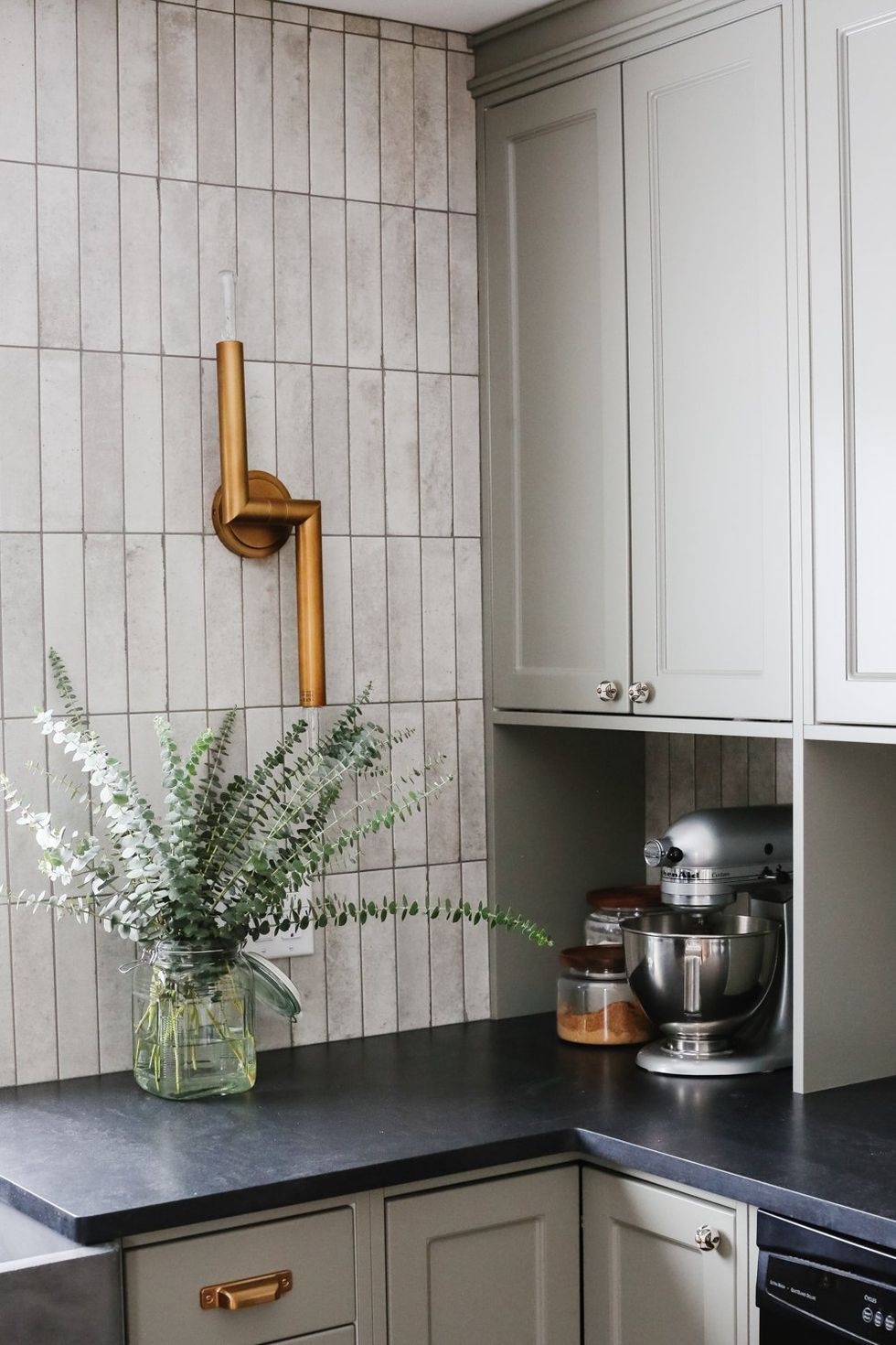 Modern kitchen corner with white cabinets, black countertop, wood wall decor, and a vase of greenery