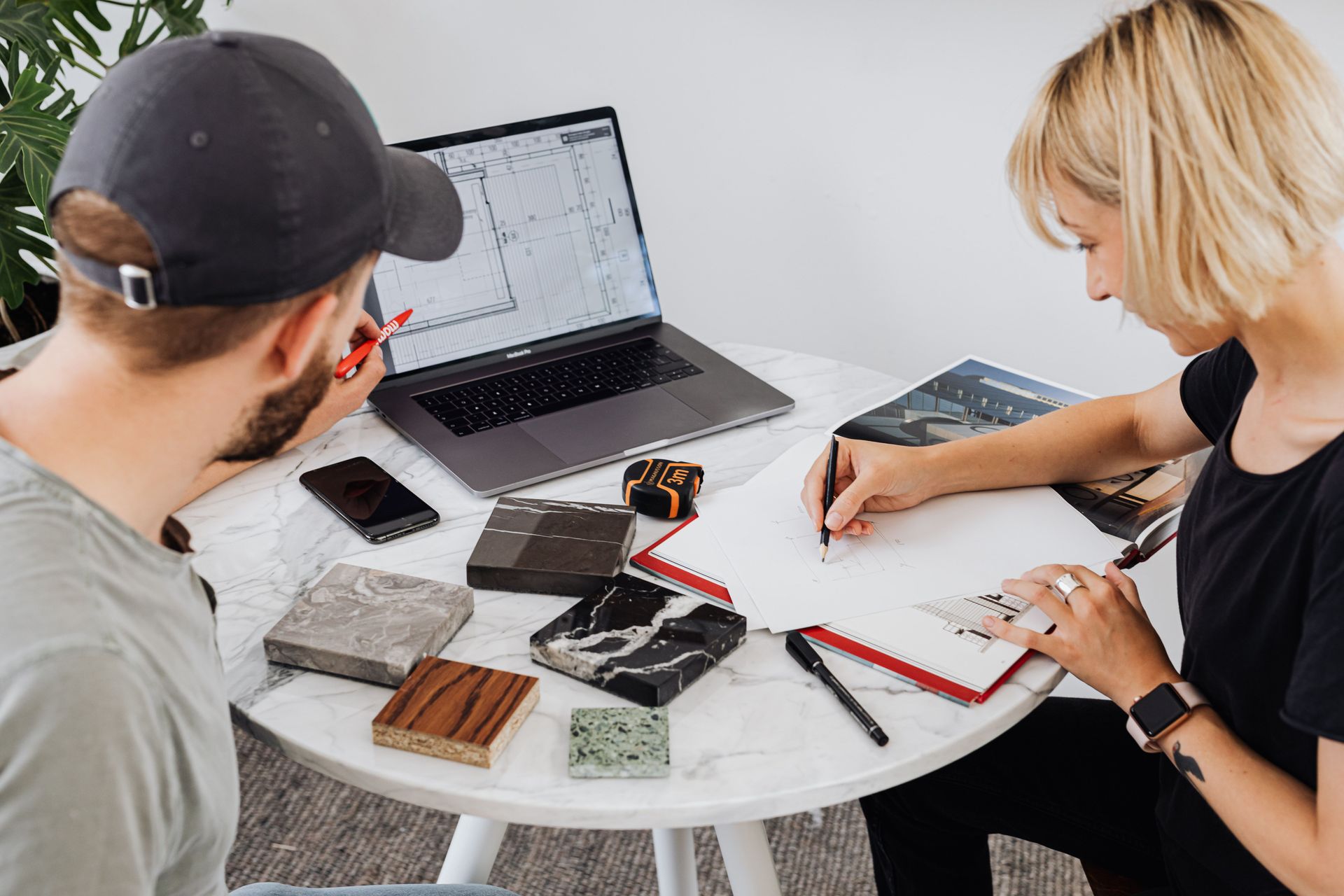 Two people reviewing fabric samples and sketches at a table with a laptop in a design workspace