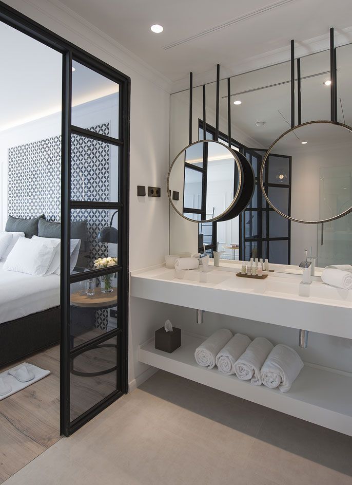 Modern bathroom vanity with round mirrors, white countertop, and open shelf with rolled towels