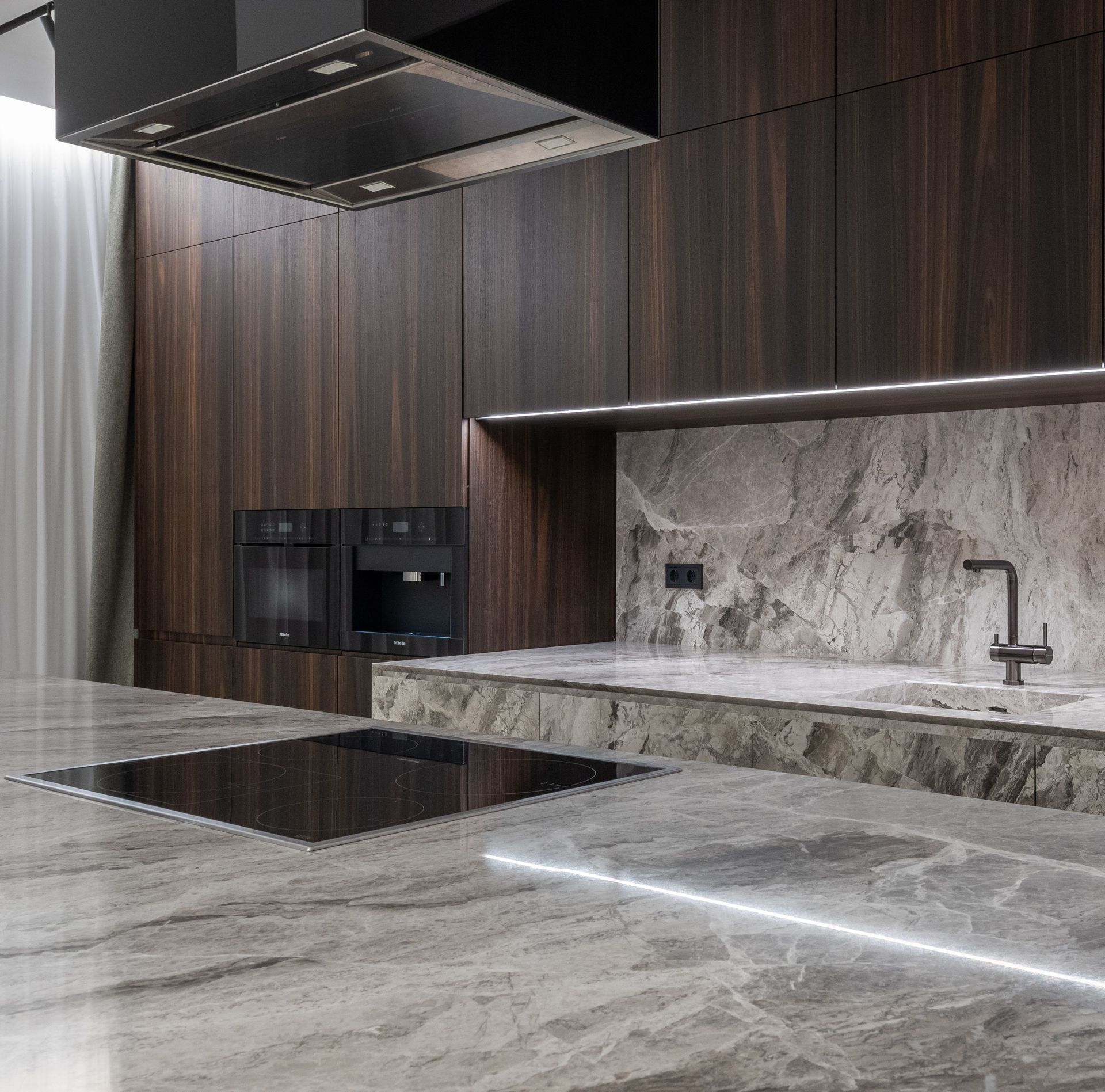 Modern kitchen with dark wood cabinets, marble counters, and sleek built-in appliances