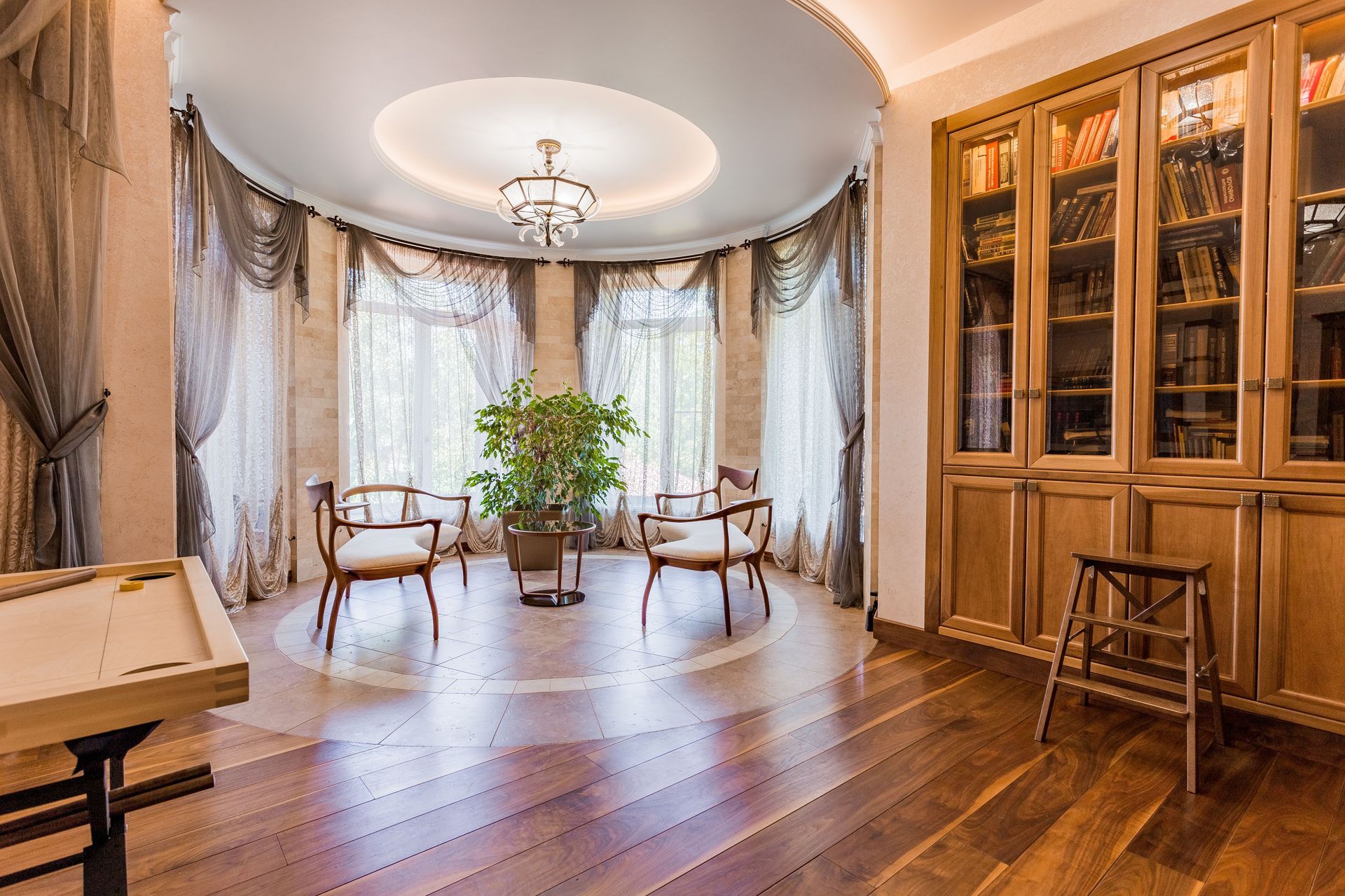 Elegant living room with curved window seating, wooden cabinets, and a grand piano near tall windows