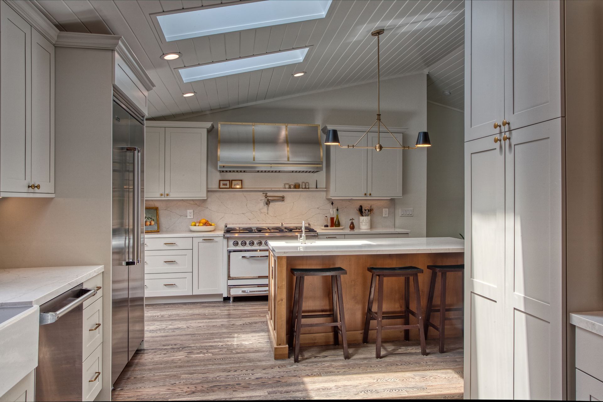 Bright white kitchen with skylights, island seating, stainless stove, and hardwood floors