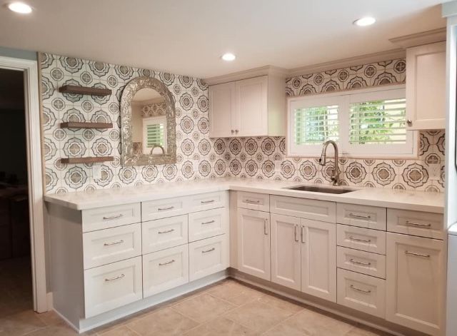 Minimalist kitchen with white cabinets, brass fixtures, shelves, and pale pink patterned tile backsplash.
