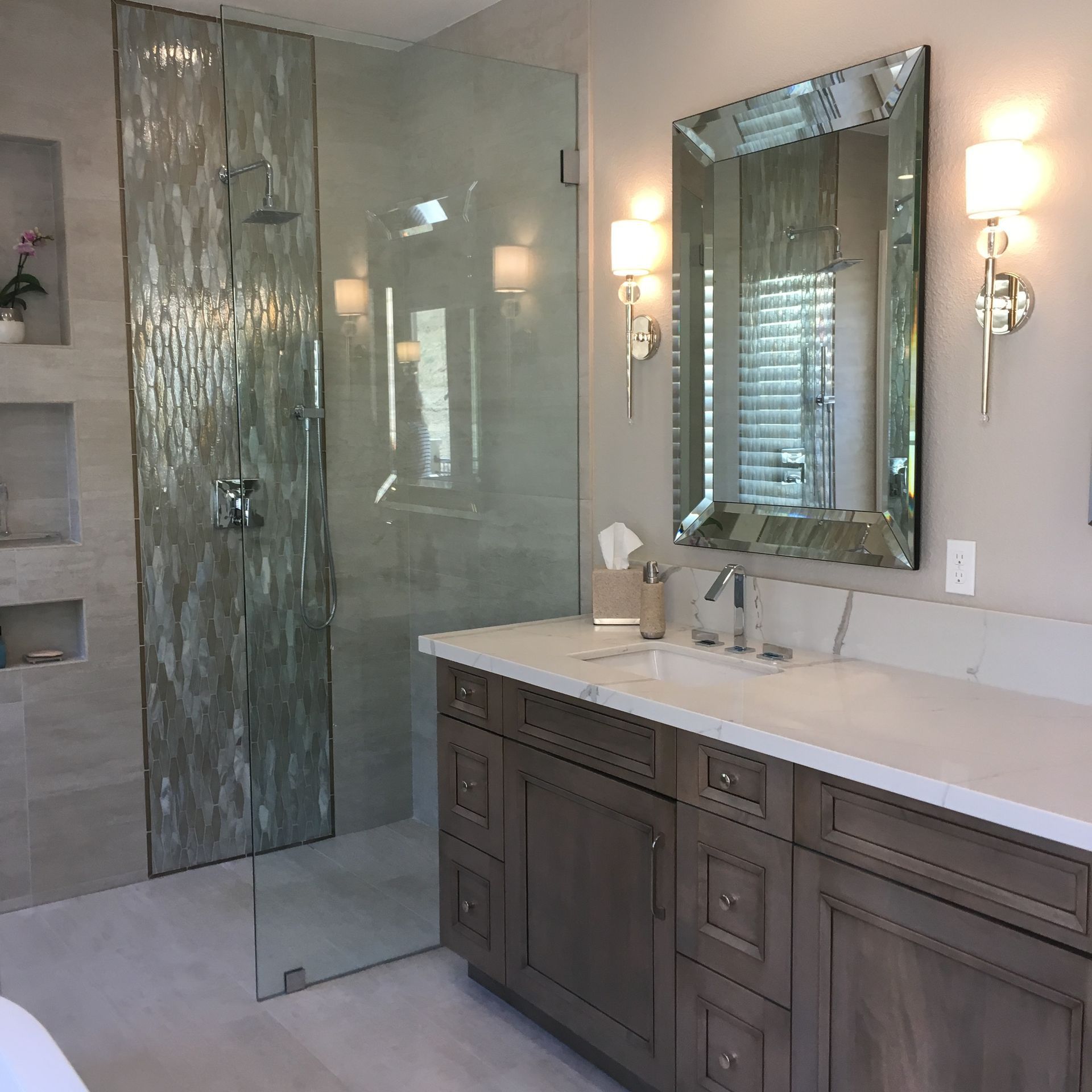 Elegant bathroom with glass shower, double vanity, mirror, and wall sconces