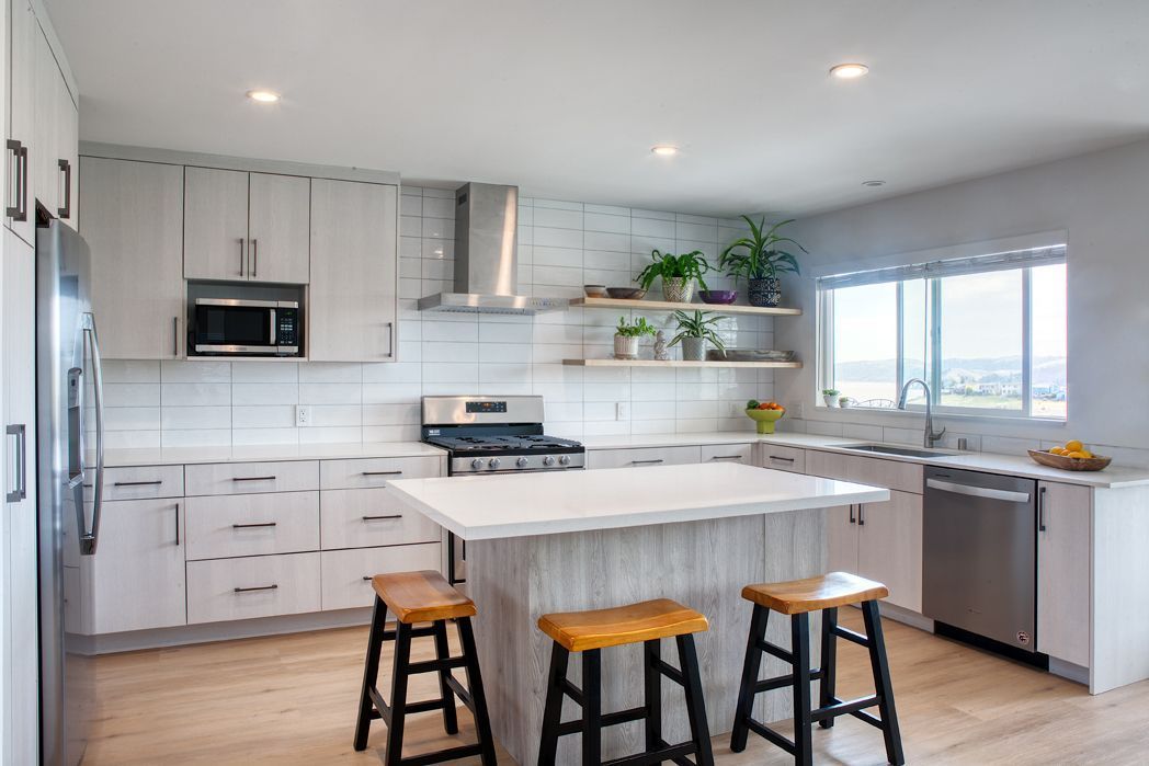 Modern kitchen with dark cabinetry, black stools, tiled backsplash, and potted herbs on the counter