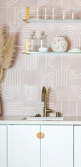 Minimalist kitchen with white cabinets, brass fixtures, shelves, and pale pink patterned tile backsplash.