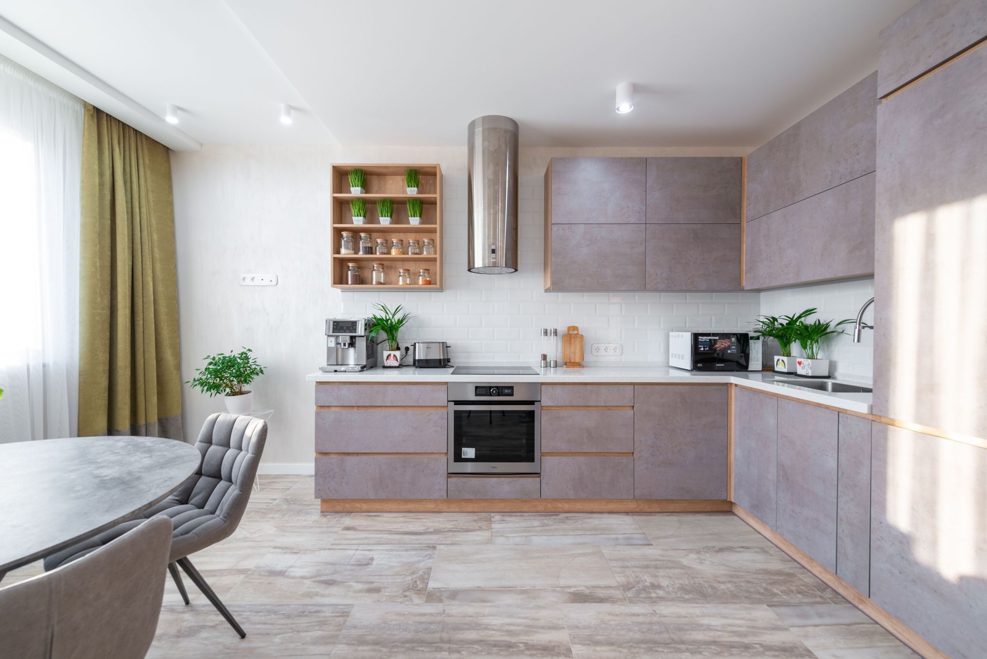 Bright modern kitchen with gray cabinets, wood accents, dining table, and large window curtains