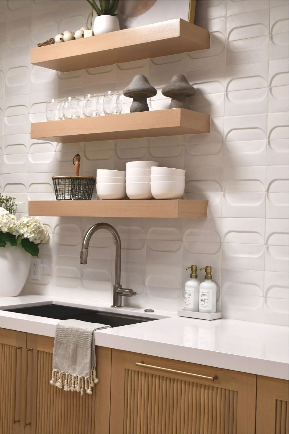 Modern kitchen sink area with floating wood shelves, white tiles, and neatly arranged dishes and bottles