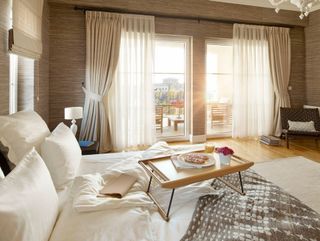 Bright bedroom with large windows, white bed, wooden coffee table, and balcony view through sheer curtains