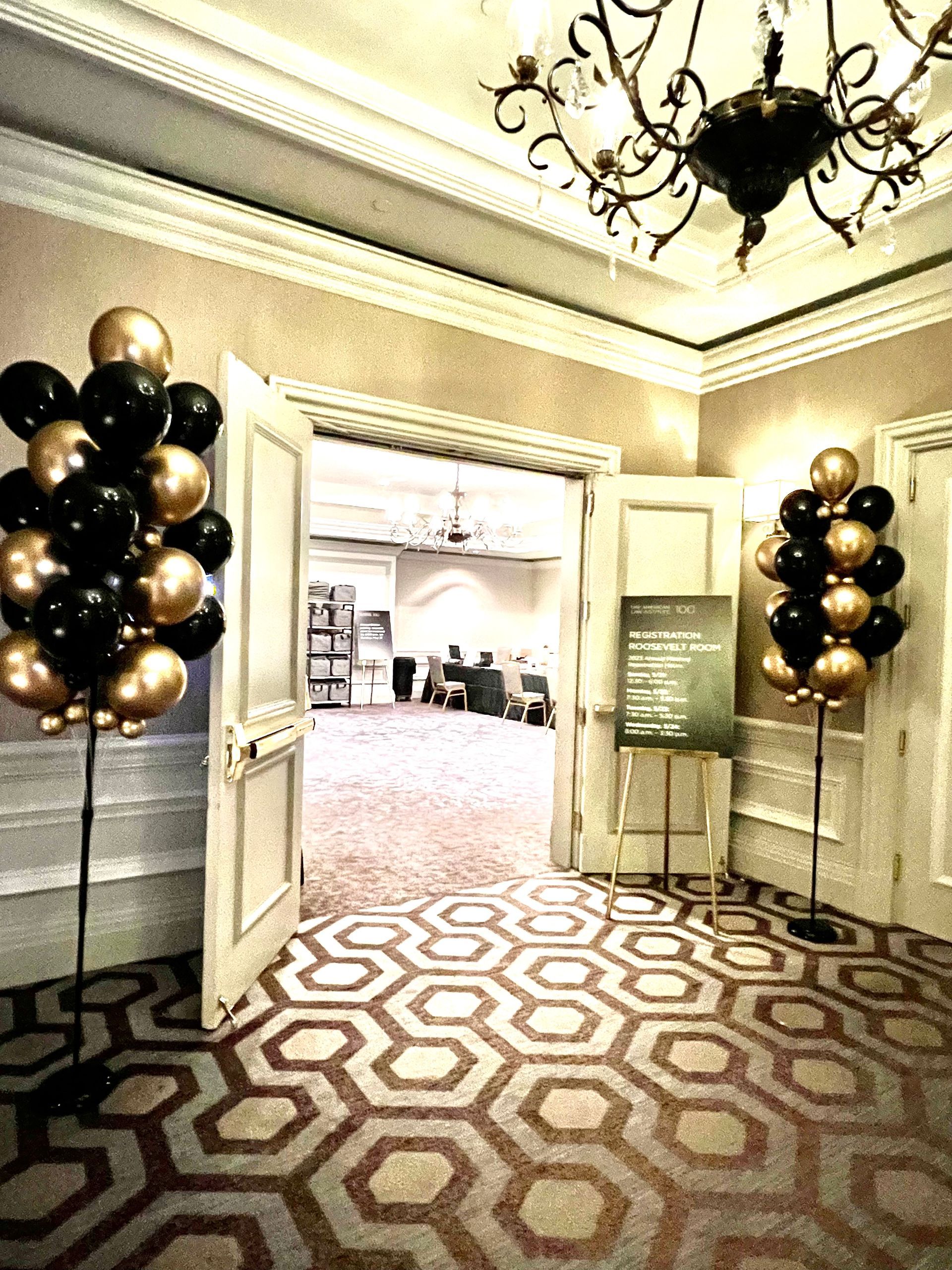A hallway with black and gold balloons and a chandelier.