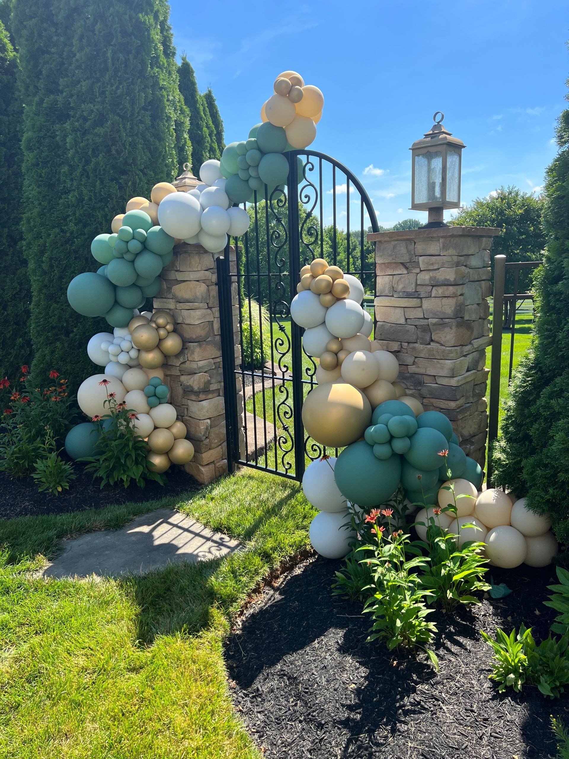 A gate decorated with balloons in front of a stone wall.