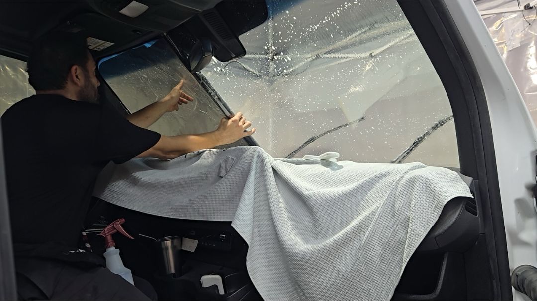 Person in a vehicle covering a shattered windshield with a white blanket during repairs