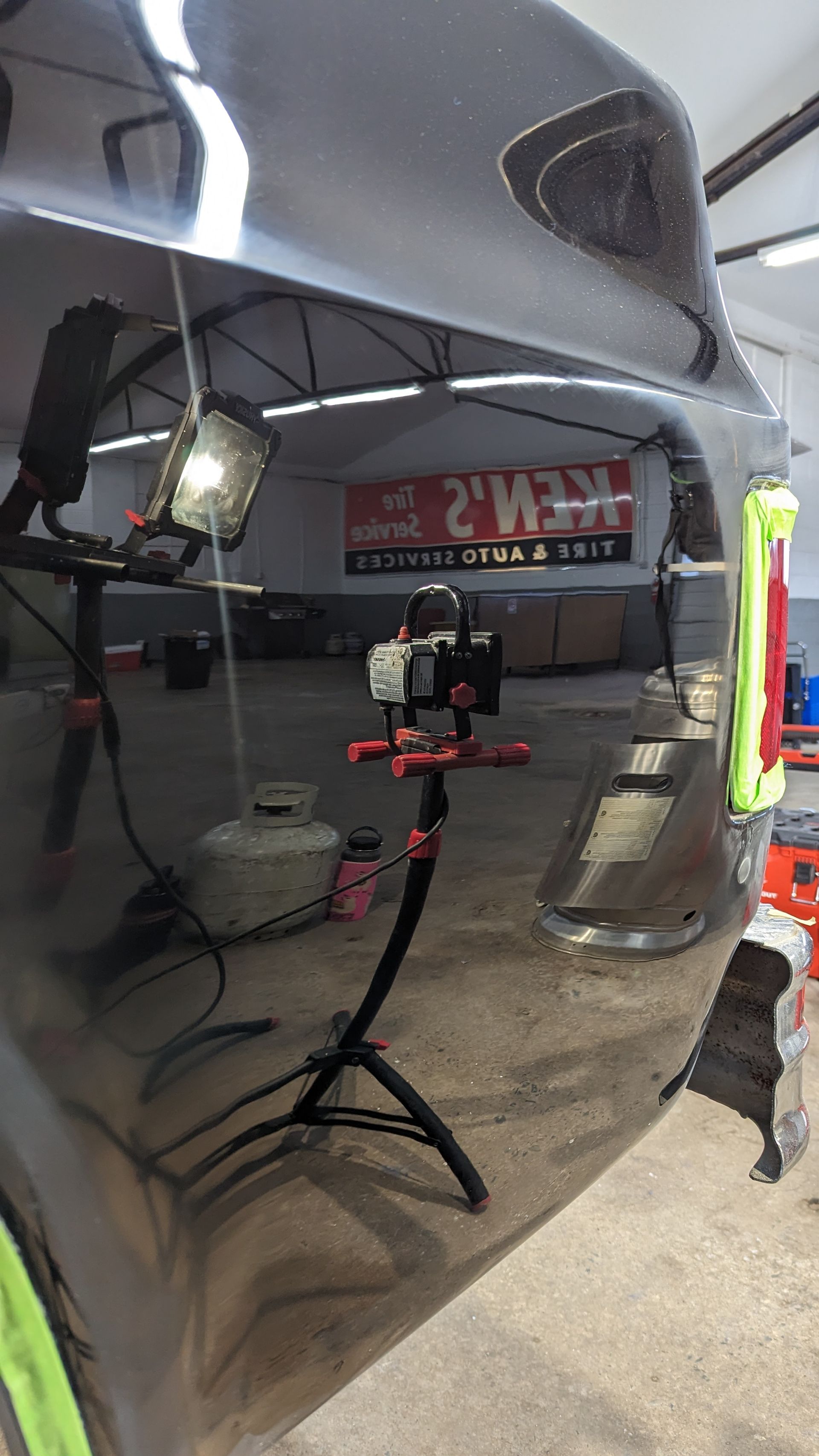 Car's glossy side panel reflecting a garage with tools, lights, and a sign in the background