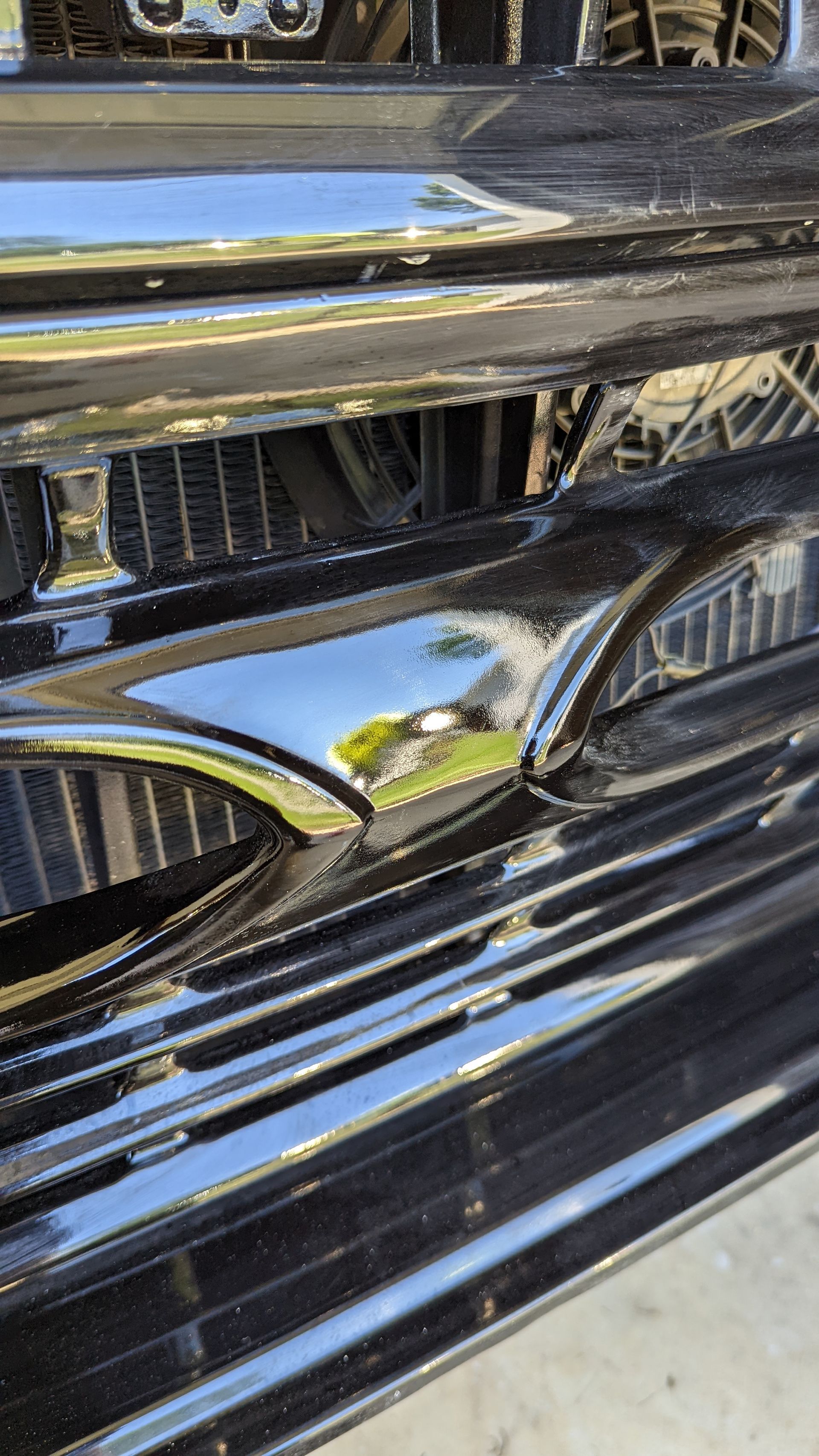 Close-up of a shiny black car grille and headlight reflecting the surroundings.