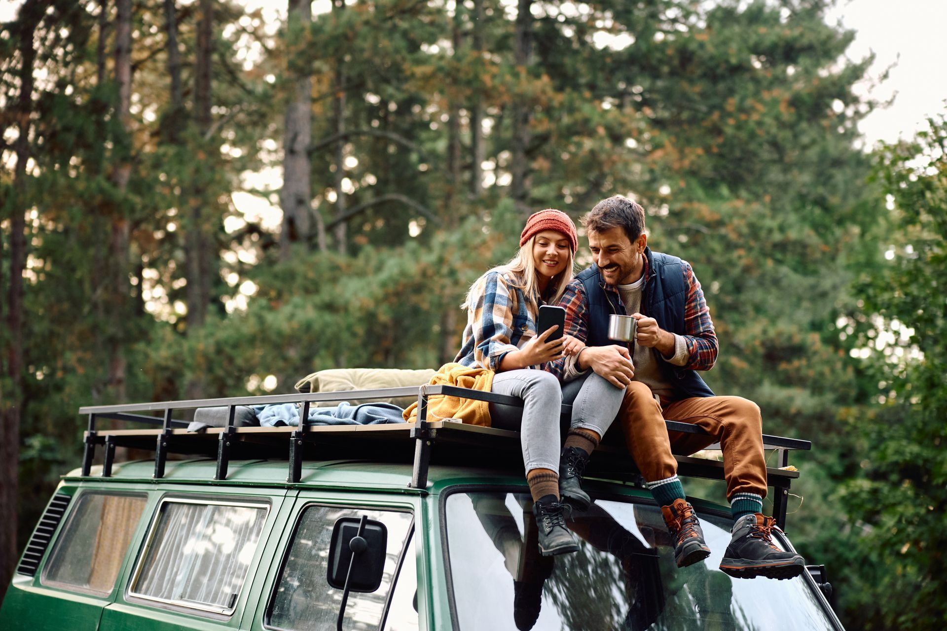 Two people sitting on top of a green off-road vehicle in a forest, smiling and chatting.