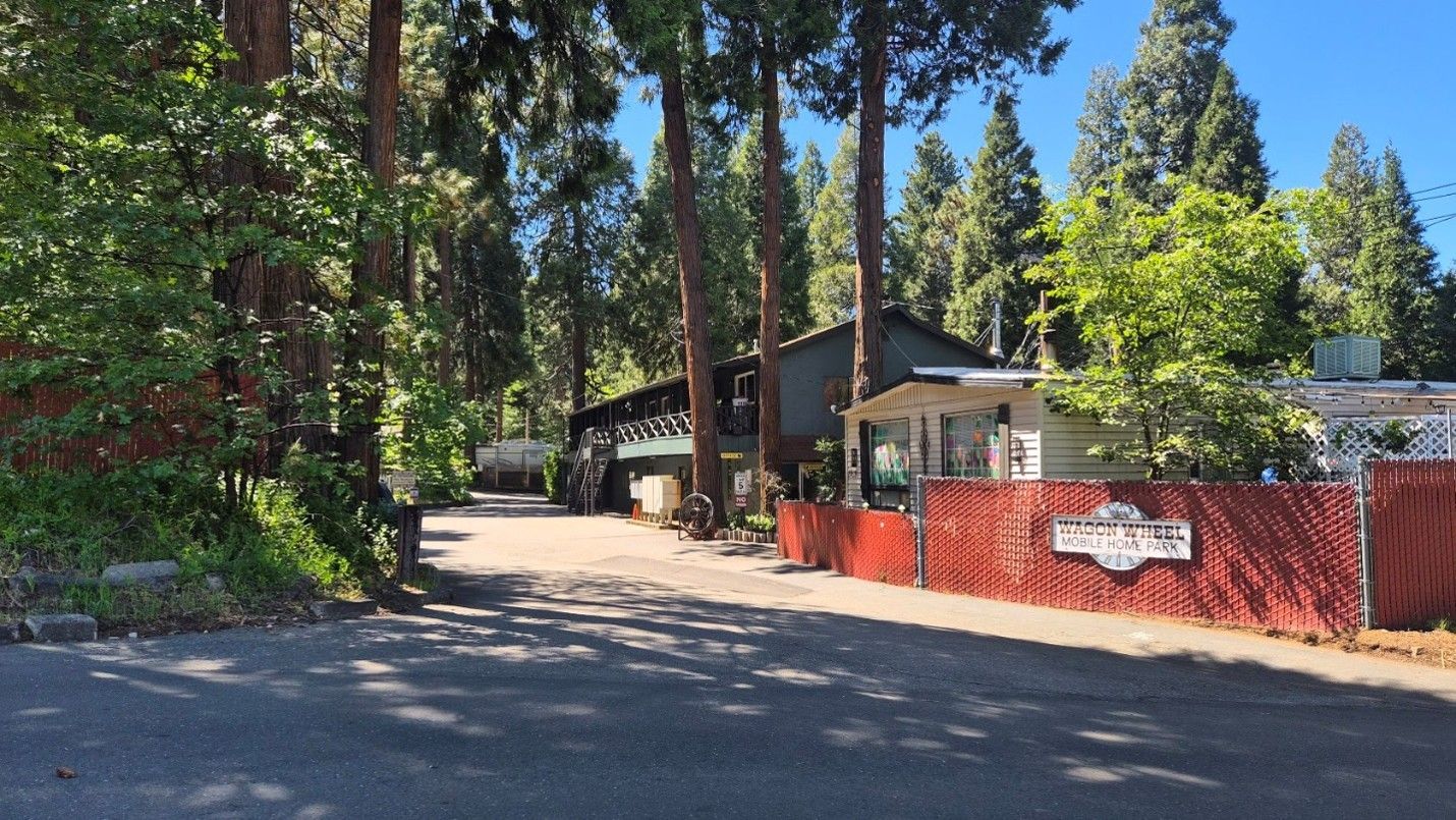 Tree-lined driveway beside a red fence and small building in a wooded residential area.