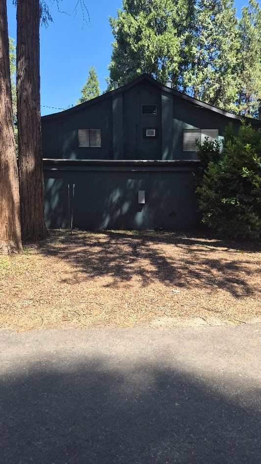 Dark house with a two-car garage under tall trees, viewed from a street