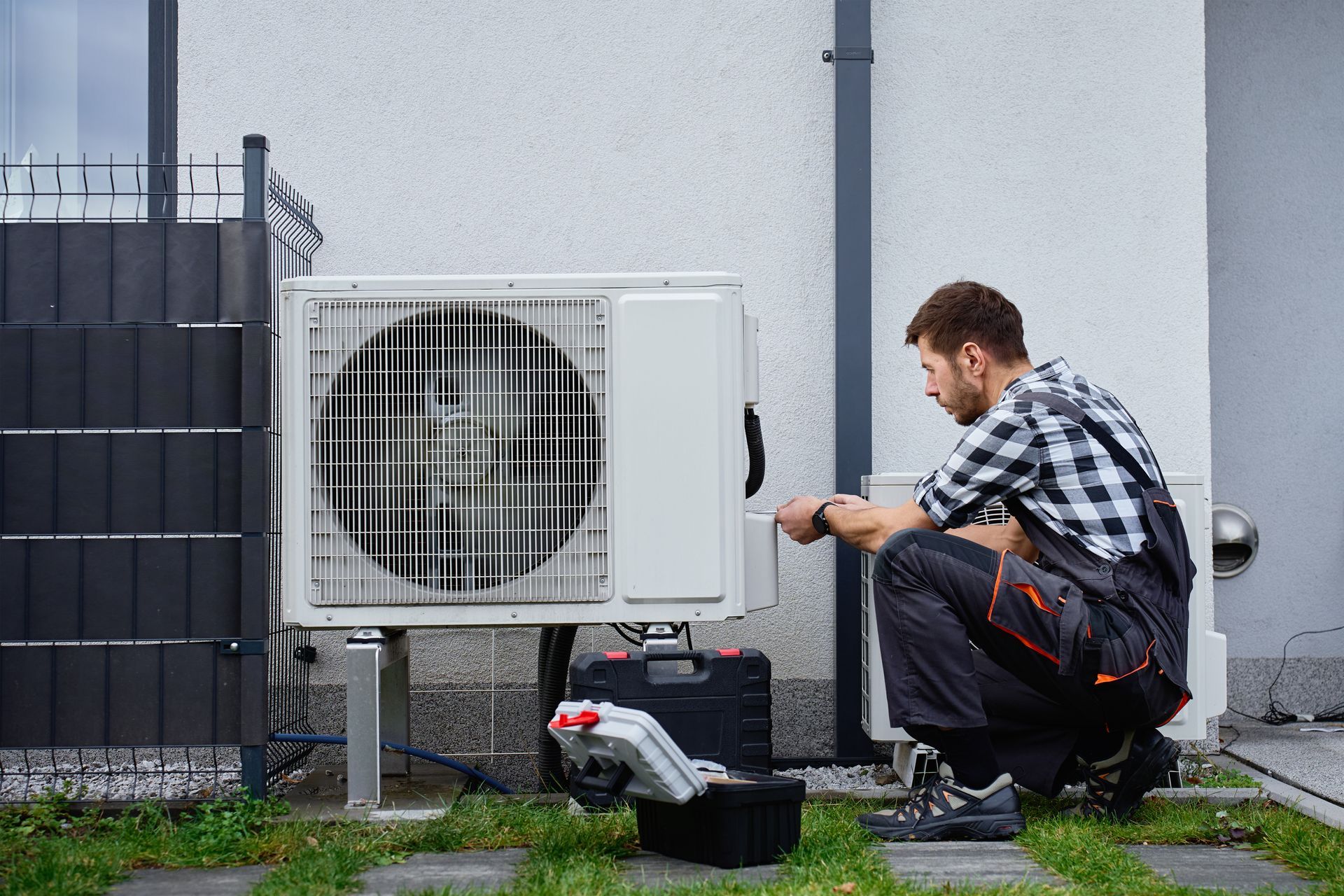 Technician performing maintenance on outdoor heat pump unit near residential building exterior.