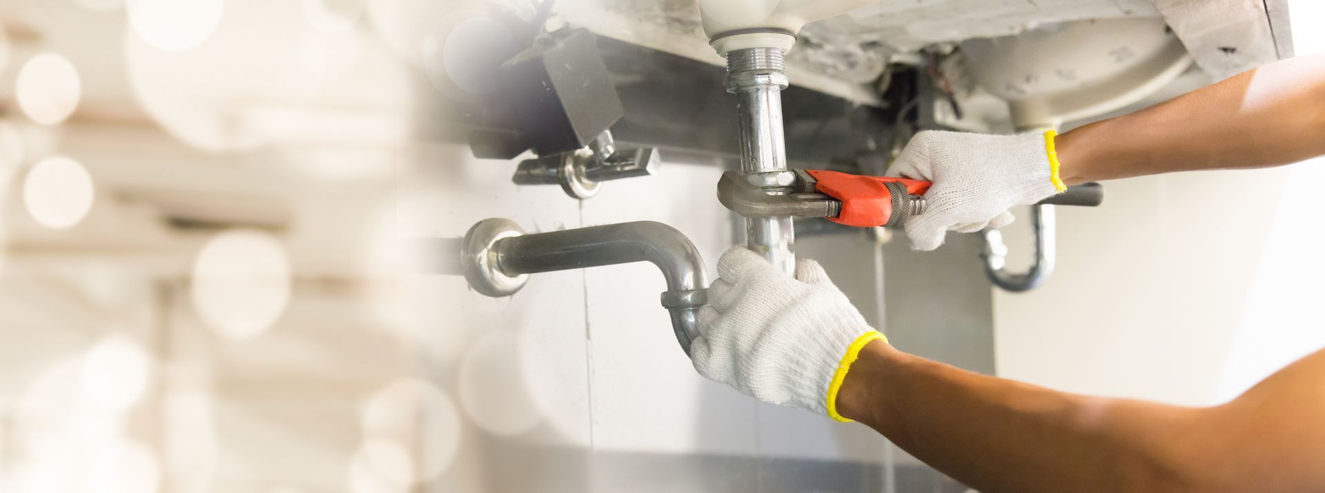 Expert technician providing plumbing services by tightening a metal sink pipe with a wrench.