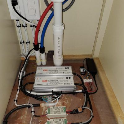 A bunch of wires are connected to a pipe under a sink.