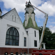 A fire truck with a raised ladder reaches the steeple of a white church on a cloudy day.