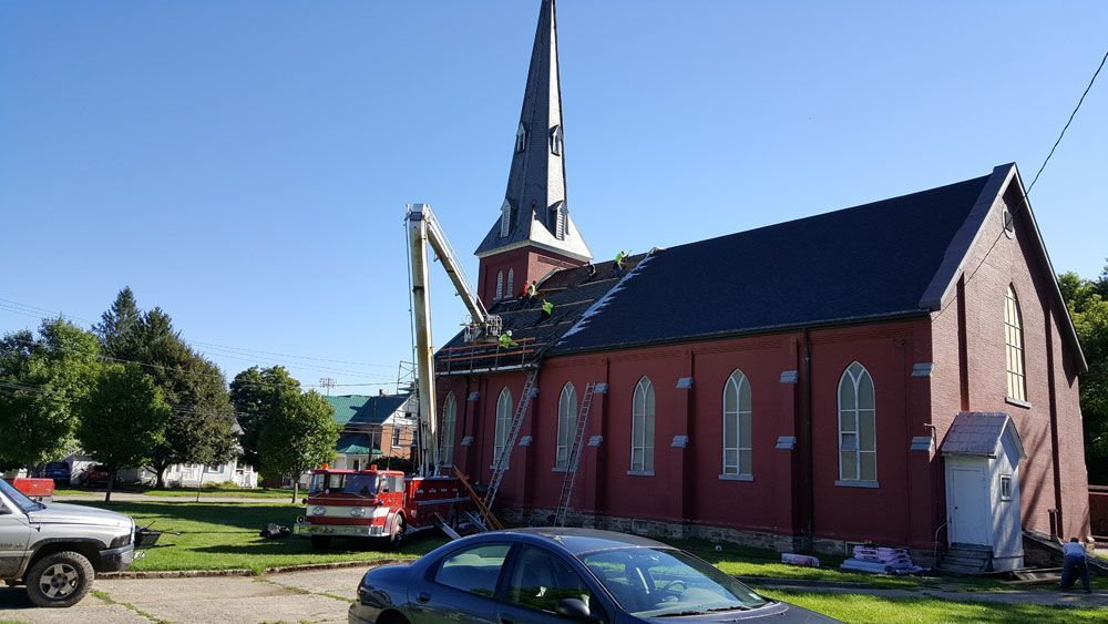 A fire truck with an extended ladder works on the damaged roof of a red brick church under a clear blue sky.