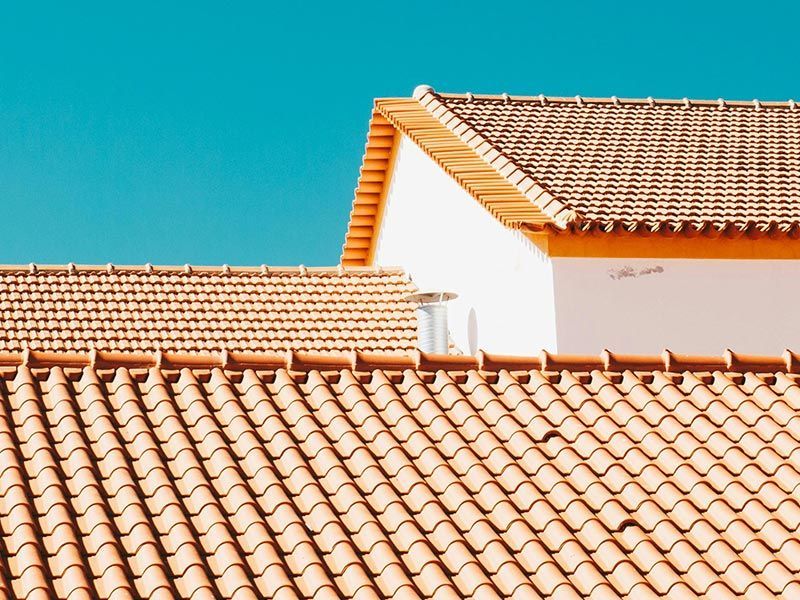 Terracotta roof tiles on two buildings under a bright, clear blue sky.