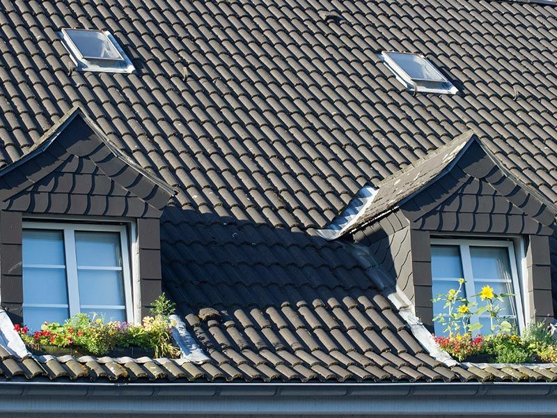 A dark-tiled roof featuring two dormer windows with flower boxes and two smaller skylights above.