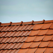 A split view of a roof showing a weathered, darker tiled section on the left and a clean, vibrant orange tiled section.