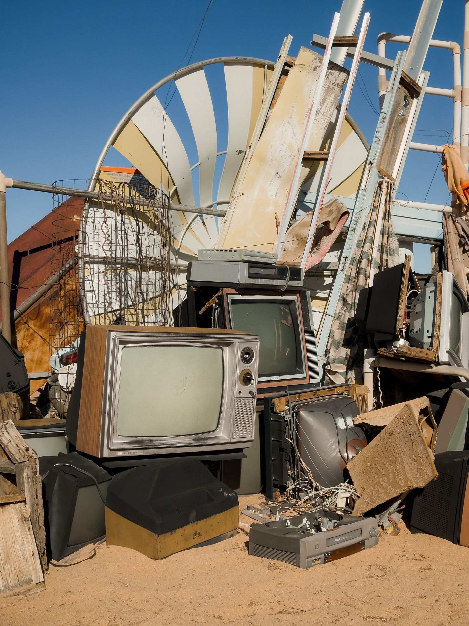 Sunlit junkyard with an old TV, metal scraps, and a large striped satellite dish in the background